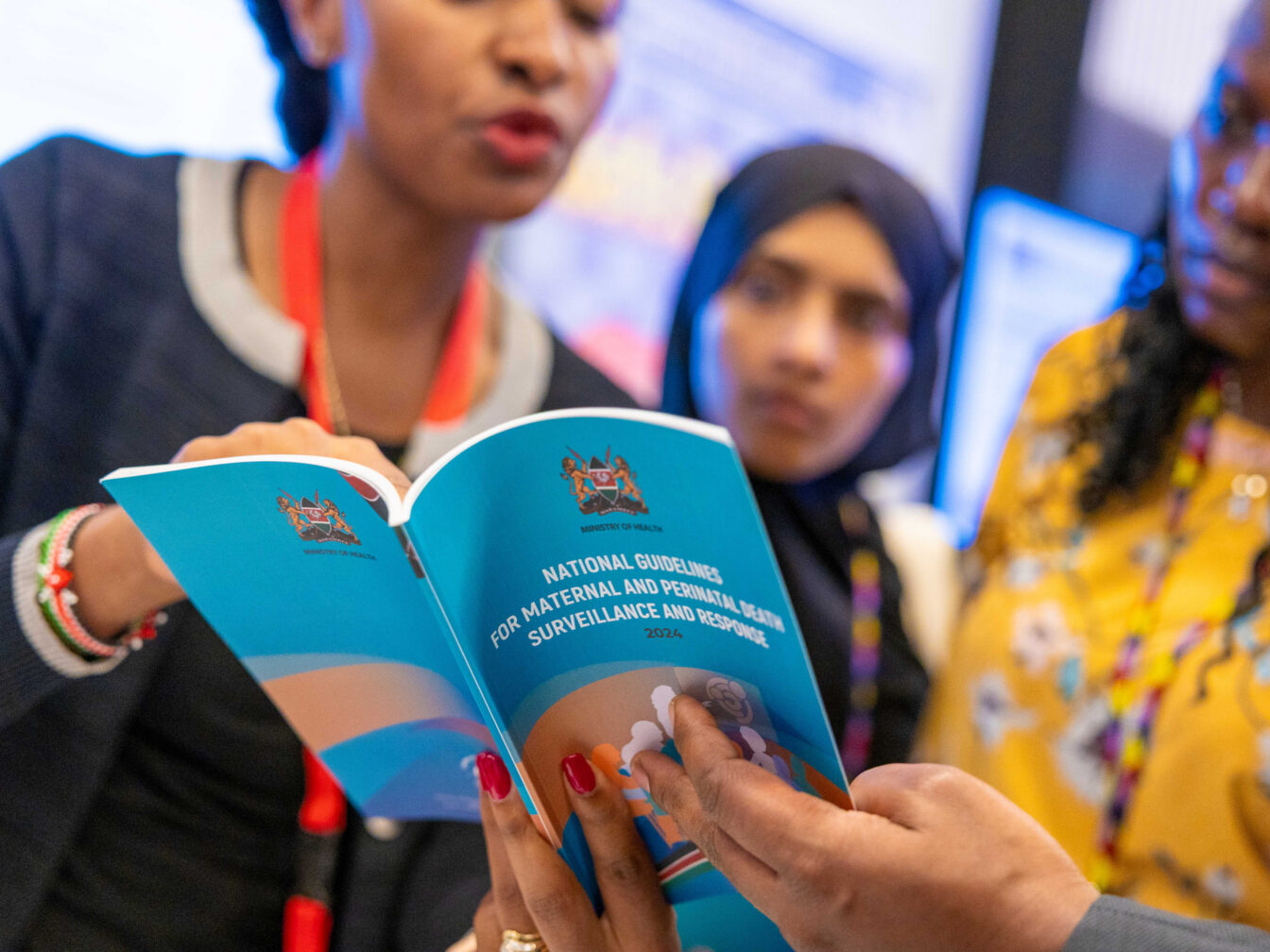 Three attendees read the National Guidelines for Maternal and Perinatal Death Surveillance and Response in the country showcase at the International Maternal and Newborn Health Conference 2026